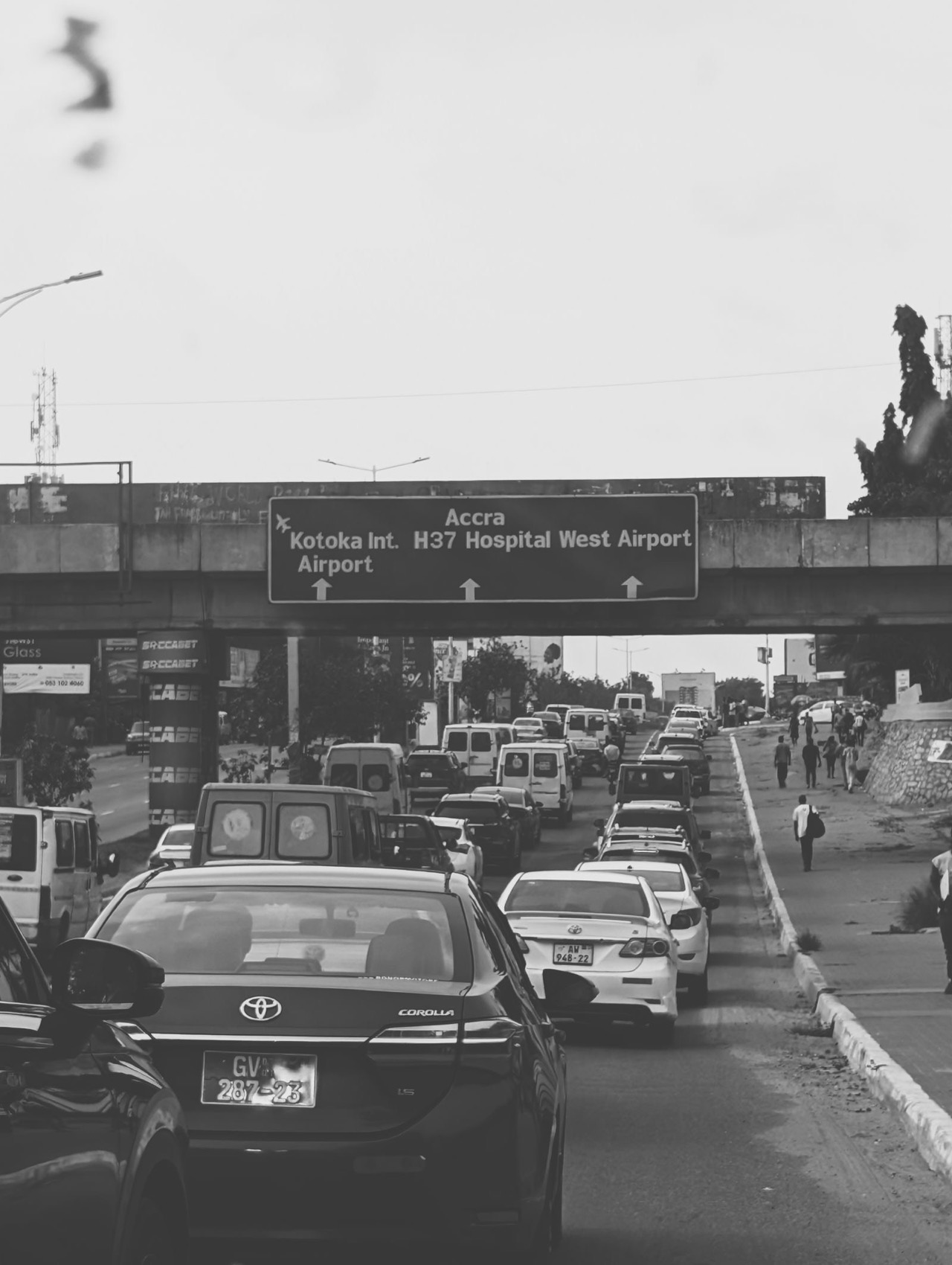 Traffic queuing in Accra beneath an overhead sign pointing to Kotoka International Airport
