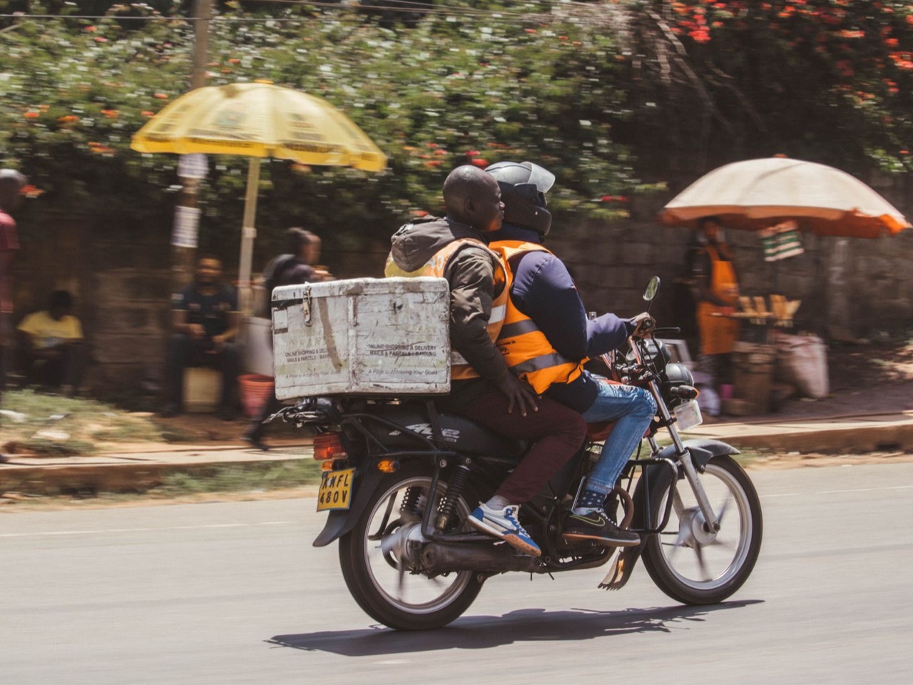 A courier riding a motorbike through city traffic with a large delivery box mounted behind the seat