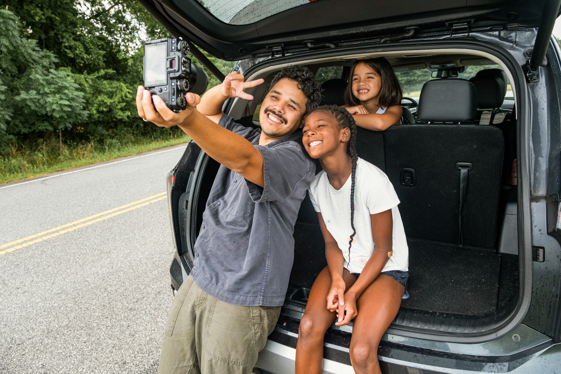 A family smiling together beside their car