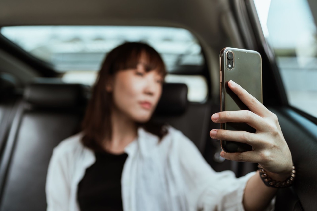 A passenger sitting in the back seat of a car, holding up her phone
