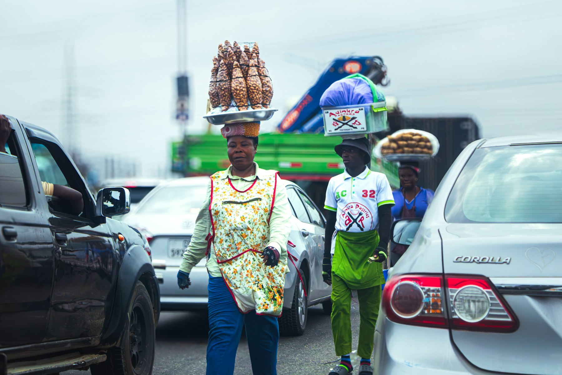 Street traders in Accra carrying trays of packaged snacks and pastries on their heads between cars in traffic